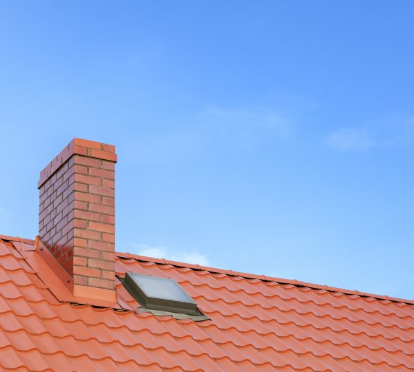 Roof with ceramic tile chimney against blue sky, space for text.